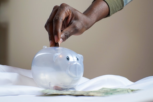 person putting a coin in a clear piggy bank